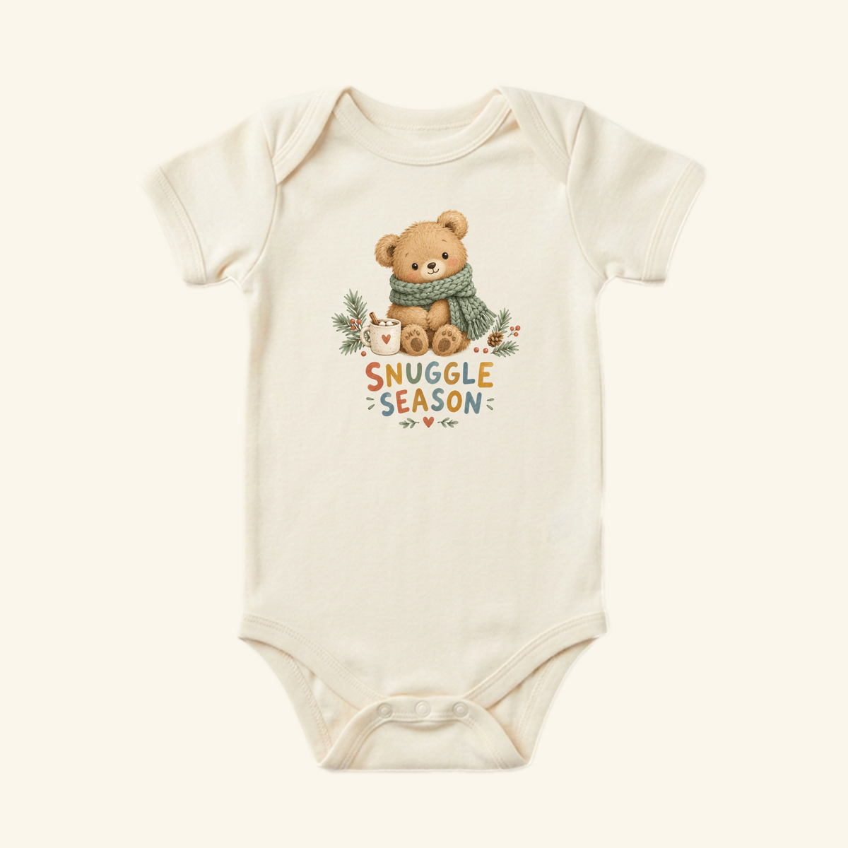 Cream-colored Toodleroos Snuggle Season Baby Onesie featuring an illustration of a teddy bear wearing a green scarf and holding a mug with the text Snuggle Season below.