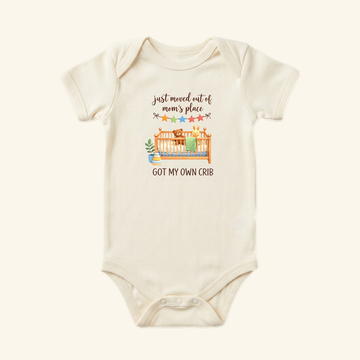 Cream-colored Funny Baby Onesie – Got My Own Crib Bodysuit featuring an illustration of a crib with a teddy bear and rabbit, with the text Just moved out of mom’s place and GOT MY OWN CRIB.
