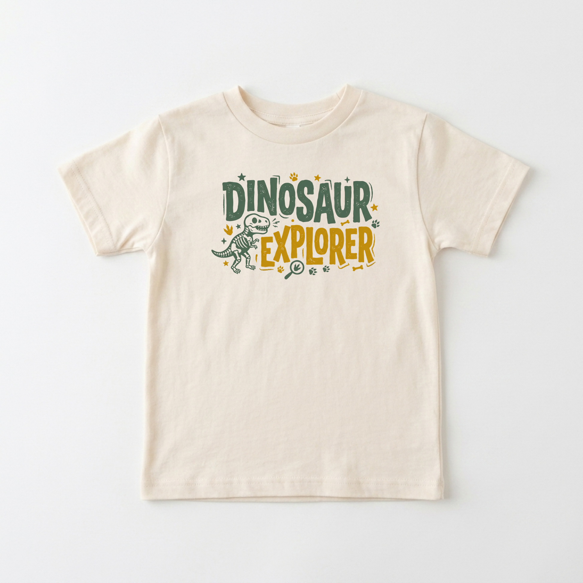 A light beige short-sleeve t-shirt with a 'Dinosaur Explorer' graphic on the chest, featuring a small dinosaur illustration and colorful text, displayed on a clean white background.