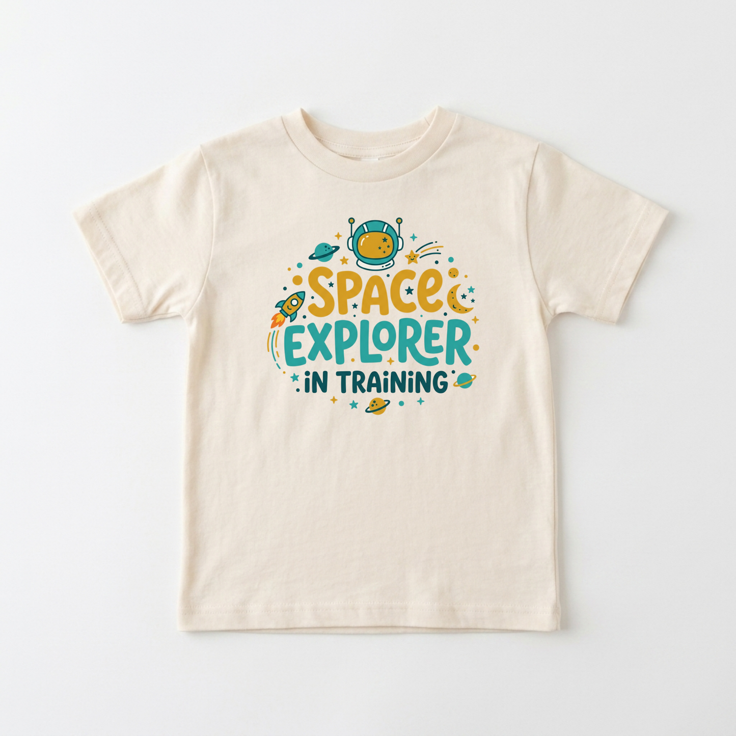 A cream-colored short-sleeve t-shirt with a colorful graphic on the front that reads 'SPACE EXPLORER IN TRAINING' in yellow and teal lettering with cartoon space elements, shown on a light gray background.