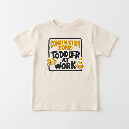 A cream-colored toddler short-sleeve t-shirt with a 'Construction Zone: Toddler at Work' graphic on the chest, displayed flat against a light gray background.