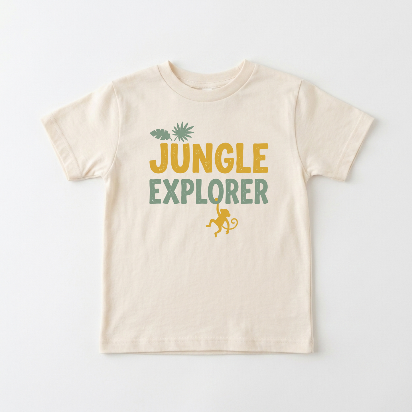 A cream-colored short-sleeve t-shirt with a 'JUNGLE EXPLORER' graphic on the chest, featuring a yellow-green monkey and palm tree design, laid flat against a white background.