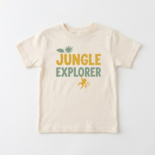 A cream-colored short-sleeve t-shirt with a 'JUNGLE EXPLORER' graphic on the chest, featuring a yellow-green monkey and palm tree design, laid flat against a white background.