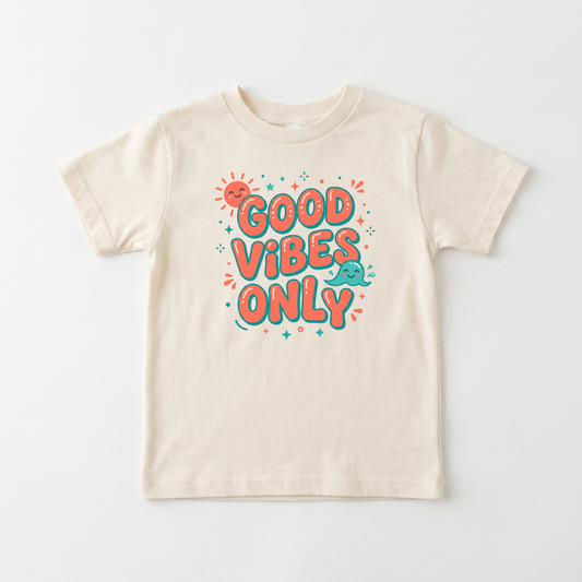 A cream-colored short-sleeve t-shirt with a colorful graphic on the front that reads 'GOOD VIBES ONLY' in bubbly orange letters with teal outlines, accompanied by a small smiling sun and teal cloud.