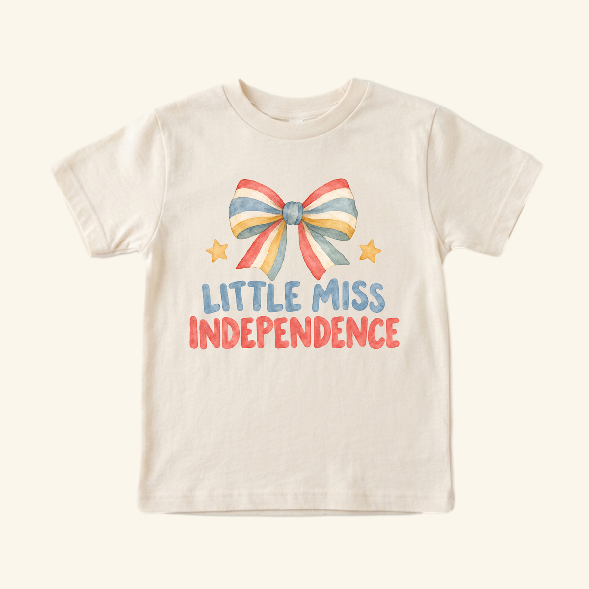 Cream-colored Little Miss Independence Toddler Shirt – Patriotic Bow Tee featuring a watercolor graphic of a red, white, and blue striped bow and two small stars.