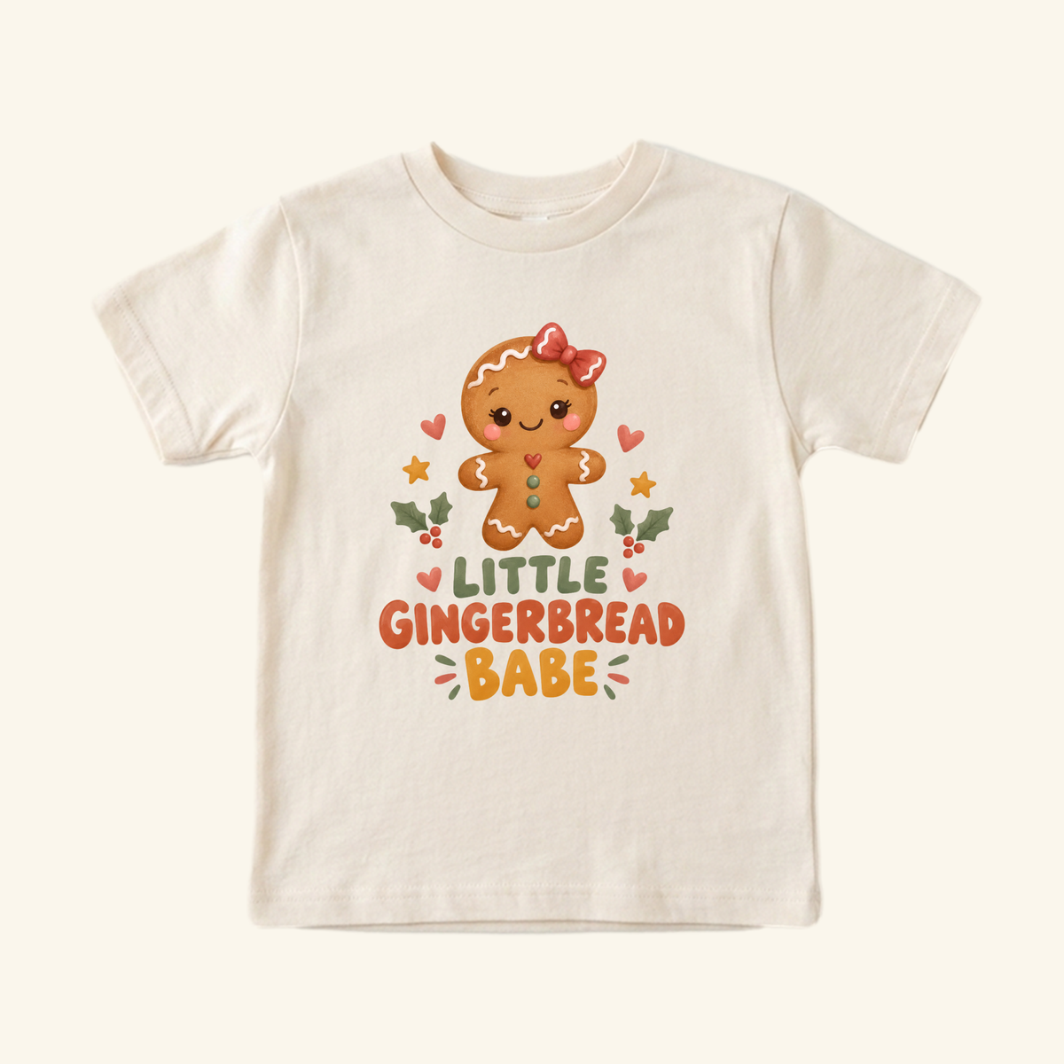 Cream-colored Little Gingerbread Babe Toddler Shirt featuring a gingerbread girl with a red bow, surrounded by hearts, stars, and holly, with the text LITTLE GINGERBREAD BABE.