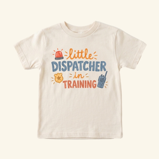 Cream-colored Little Dispatcher in Training Toddler Shirt featuring a red siren, gold badge, and walkie-talkie illustrations, making for a perfect first responder gift.