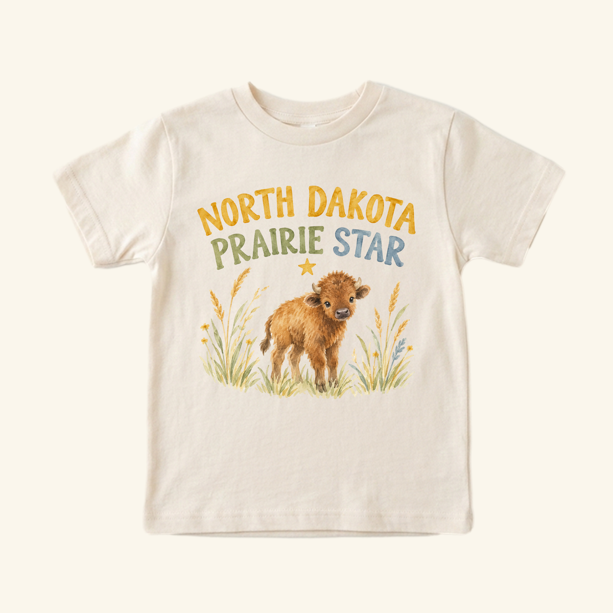 Cream-colored North Dakota Toddler Shirt – Prairie Star Baby Bison Tee featuring a watercolor illustration of a bison calf in a grassy field beneath the text NORTH DAKOTA PRAIRIE STAR and a small yellow star.