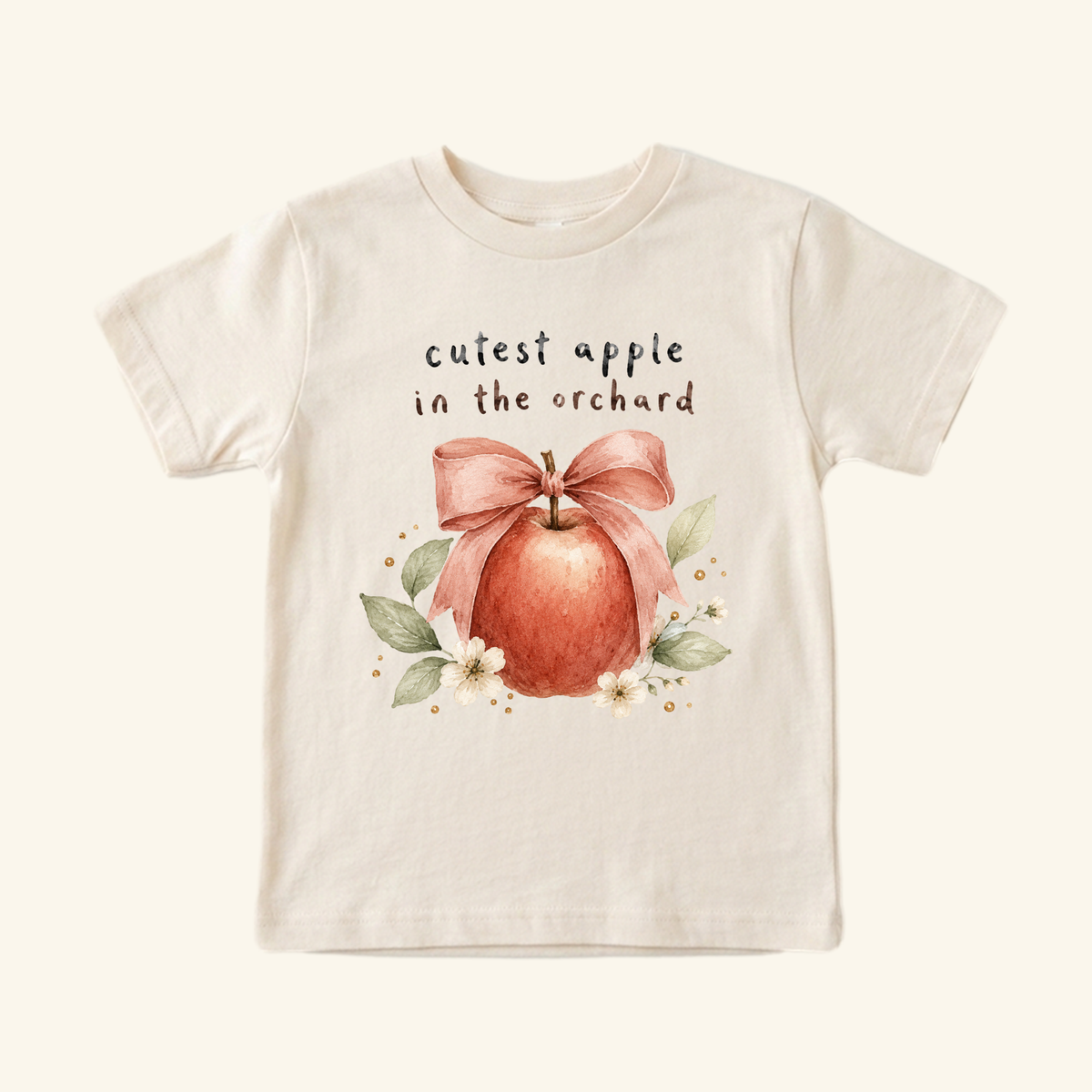 Toodleroos Cutest Apple in the Orchard Toddler Shirt – Fall Apple Bow Tee featuring a cream-colored toddler shirt with a watercolor illustration of an apple tied with a pink bow, surrounded by flowers, leaves, and the text cutest apple in the orchard.