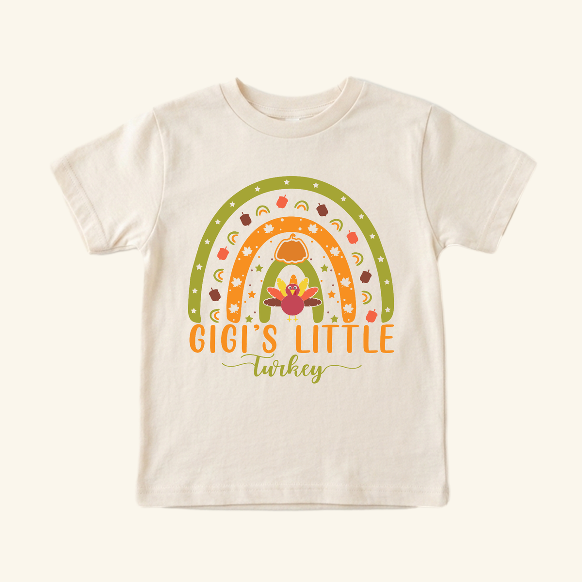 Cream-colored Gigi’s Little Turkey Toddler Shirt featuring a graphic of a colorful rainbow with a turkey, pumpkin, and autumn leaves, with the text Gigi’s Little Turkey below.