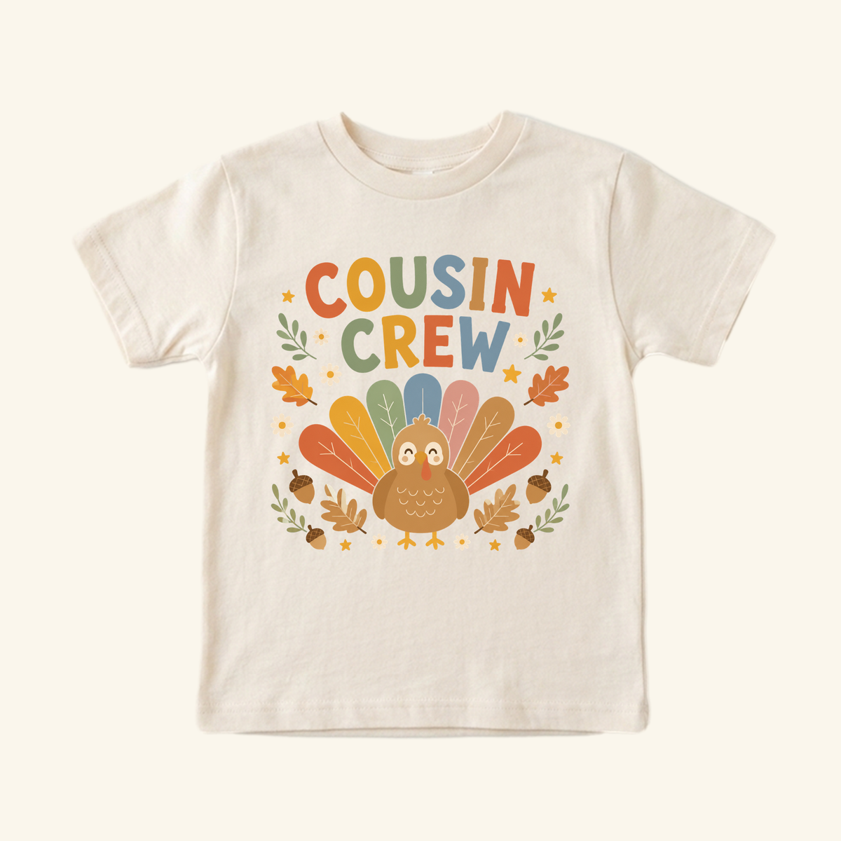 Cream Thanksgiving Cousin Shirt – Cousin Crew Turkey Toddler Tee featuring a cartoon turkey with colorful feathers and the text COUSIN CREW surrounded by autumn leaves, acorns, and flowers.