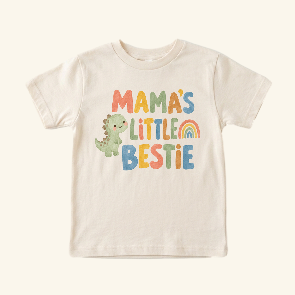 Cream Toodleroos Mama’s Little Bestie Toddler Shirt featuring a cute dinosaur and a rainbow.