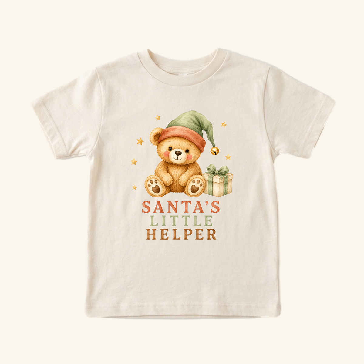 Cream-colored Santa’s Little Helper Toddler Shirt – Teddy Bear Christmas Tee featuring a teddy bear wearing a green elf hat next to a gift, with Santa’s Little Helper printed underneath.