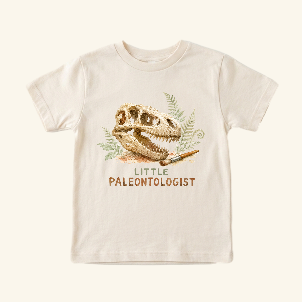 Off-white Little Paleontologist Toddler Shirt featuring a watercolor print of a T. rex fossil, a paintbrush, and the text Little Paleontologist.