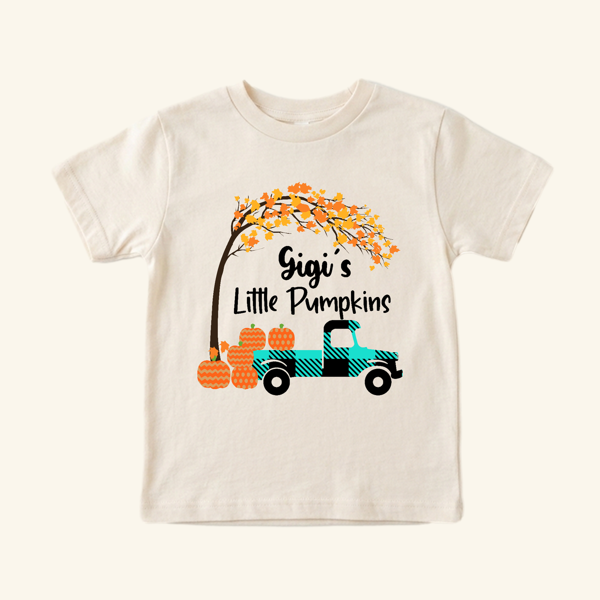 Gigi’s Little Pumpkins Toddler Shirt features a cream-colored toddler t-shirt with a turquoise plaid truck carrying pumpkins under an autumn tree and the text Gigi’s Little Pumpkins.
