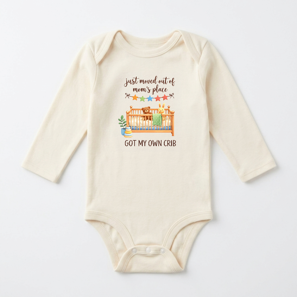 A cream-colored long-sleeve baby bodysuit with a graphic print on the front. The graphic features a cartoon illustration of a bear and rabbit in a crib with a green blanket, accompanied by the text 'just moved out of mom's place GOT MY OWN CRIB' in brown lettering.