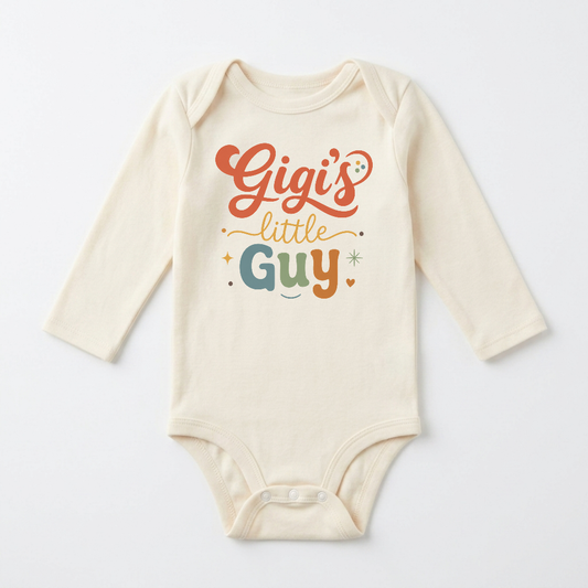 Dress your little one in the Toodleroos Long-Sleeve Gigi Baby Onesie – Gigi’s Little Guy Grandson Bodysuit, a cream-colored outfit featuring “Gigi’s little guy” playfully written in orange, green, and yellow letters with heart and star accents—an adorable gift for any grandson.