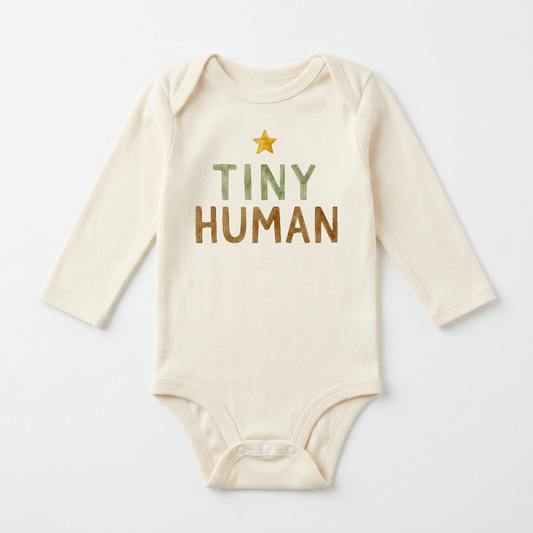 The Toodleroos Gender-Neutral Long-Sleeve Baby Onesie – Tiny Human Graphic Bodysuit is a cream-colored baby suit with long sleeves, showcasing “TINY HUMAN” in green and brown text plus a small yellow star above the lettering—a perfect minimalist choice for any little one.