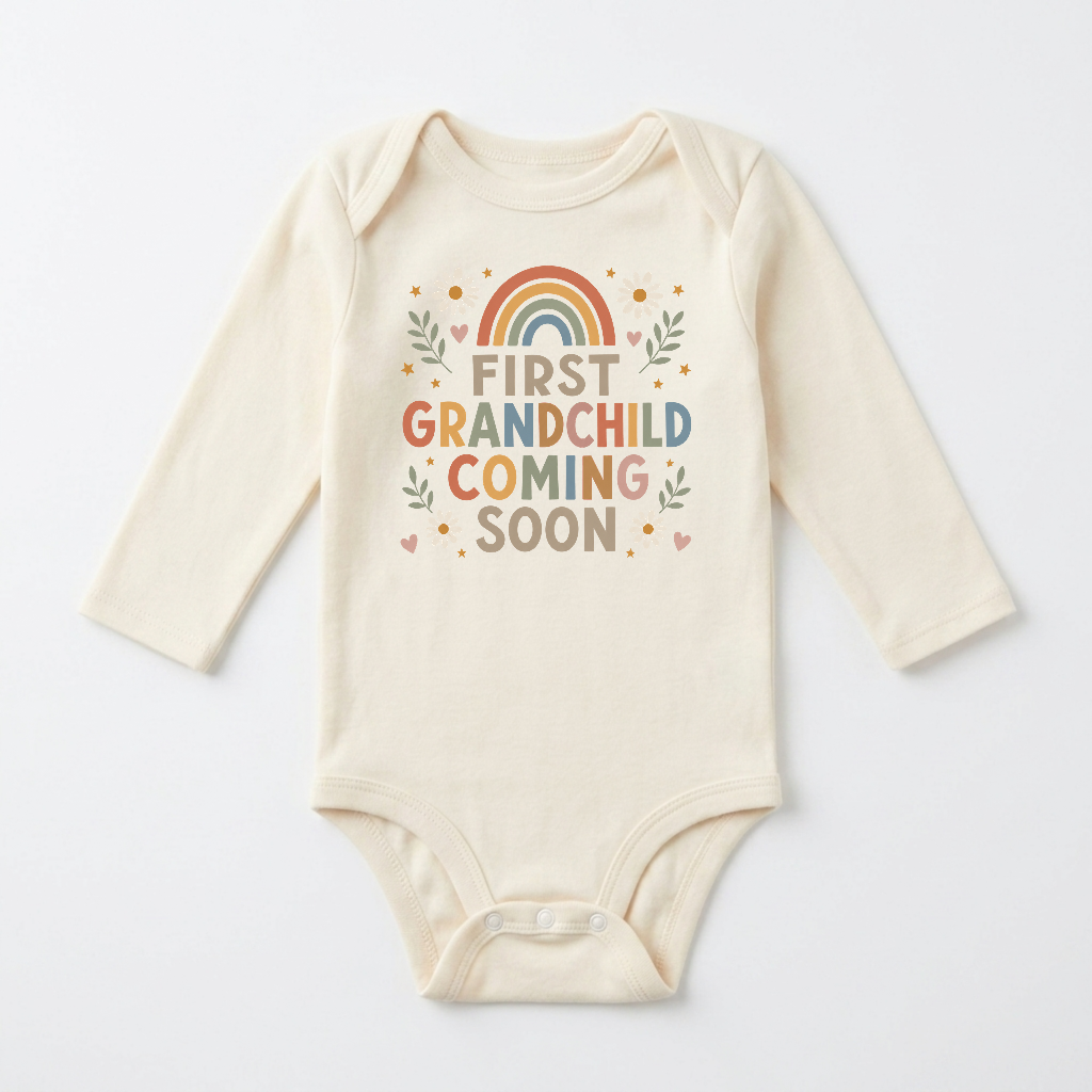 Introducing the Toodleroos Long-Sleeve First Grandchild Pregnancy Announcement Onesie – Coming Soon: a cream-colored onesie decorated with colorful “First Grandchild Coming Soon” lettering, whimsical hearts, leafy accents, and a rainbow motif above the text. This gender-neutral piece is perfect for announcing your first grandchild’s arrival or as a thoughtful pregnancy announcement.