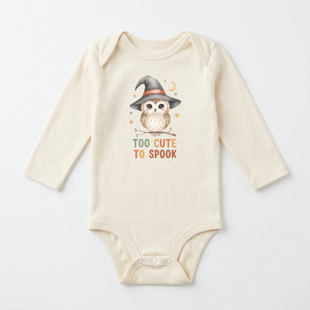 Dress your little one for their first Halloween in the Long-Sleeve Halloween Baby Onesie – Too Cute to Spook Owl Bodysuit from Toodleroos. This cream-colored baby bodysuit features a delightful illustration of an owl wearing a witch hat, surrounded by stars and a crescent moon, with the phrase “TOO CUTE TO SPOOK” printed below. An adorable and festive choice for your baby’s Halloween wardrobe!.