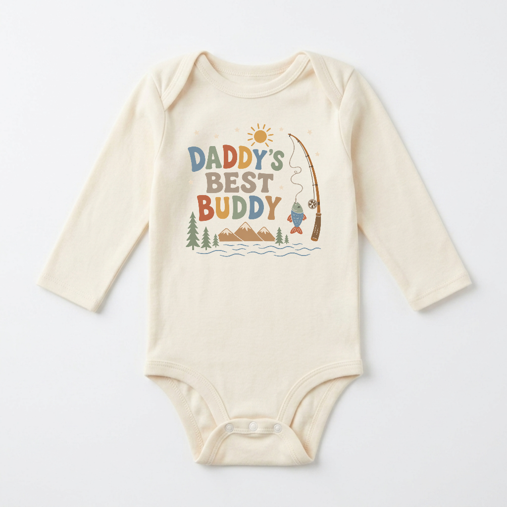 Dress your little one in the Toodleroos Long-Sleeve Baby Boy Fishing Onesie – Daddy’s Best Buddy Bodysuit. This cream-colored onesie features “Daddy’s Best Buddy” and a delightful fishing scene with mountains, trees, a river, sunshine, and a fishing pole reeling in a fish. Perfect for little outdoor adventurers, this adorable long-sleeve bodysuit is an ideal choice for celebrating the special bond between daddy and his best buddy.
