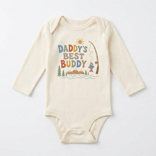 Dress your little one in the Toodleroos Long-Sleeve Baby Boy Fishing Onesie – Daddy’s Best Buddy Bodysuit. This cream-colored onesie features “Daddy’s Best Buddy” and a delightful fishing scene with mountains, trees, a river, sunshine, and a fishing pole reeling in a fish. Perfect for little outdoor adventurers, this adorable long-sleeve bodysuit is an ideal choice for celebrating the special bond between daddy and his best buddy.