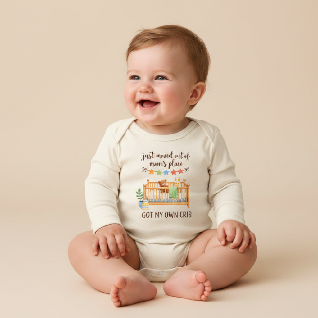 A smiling baby sits on a beige surface, dressed in the Toodleroos Funny Long-Sleeve Baby Onesie – Got My Own Crib Infant Bodysuit, featuring a playful crib illustration and the phrase “just moved out of mom’s place, got my own crib.” This adorable bodysuit is an ideal gift for welcoming a new baby.