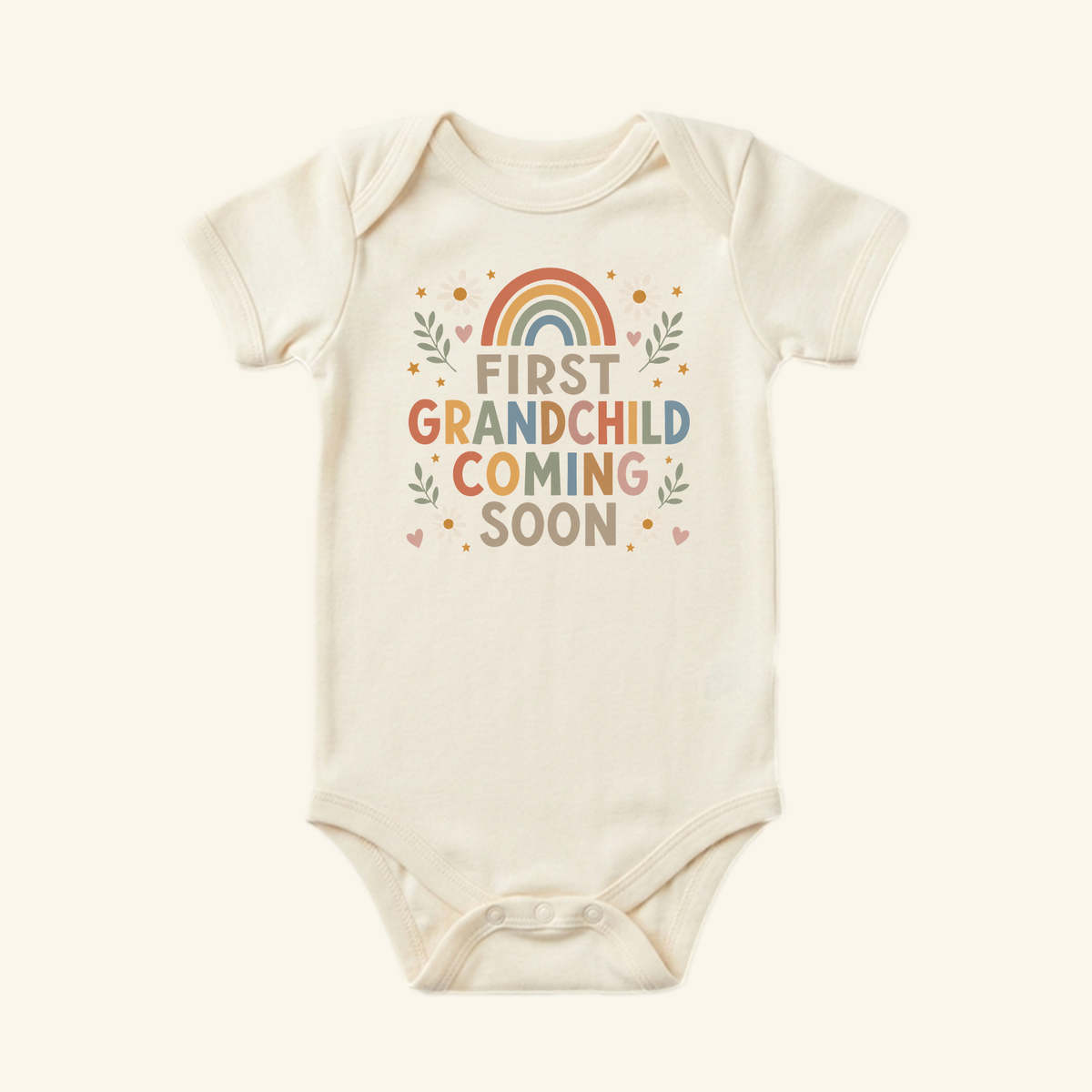 Off-white First Grandchild Announcement Baby Onesie – Coming Soon Bodysuit featuring a rainbow graphic and text surrounded by leaves, flowers, and stars, perfect for a grandparent pregnancy reveal.