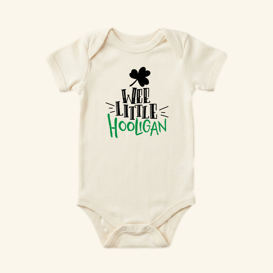Cream-colored St. Patrick’s Day Baby Onesie – Wee Little Hooligan Bodysuit featuring a black shamrock and St. Patrick’s Day-themed text in black and green.