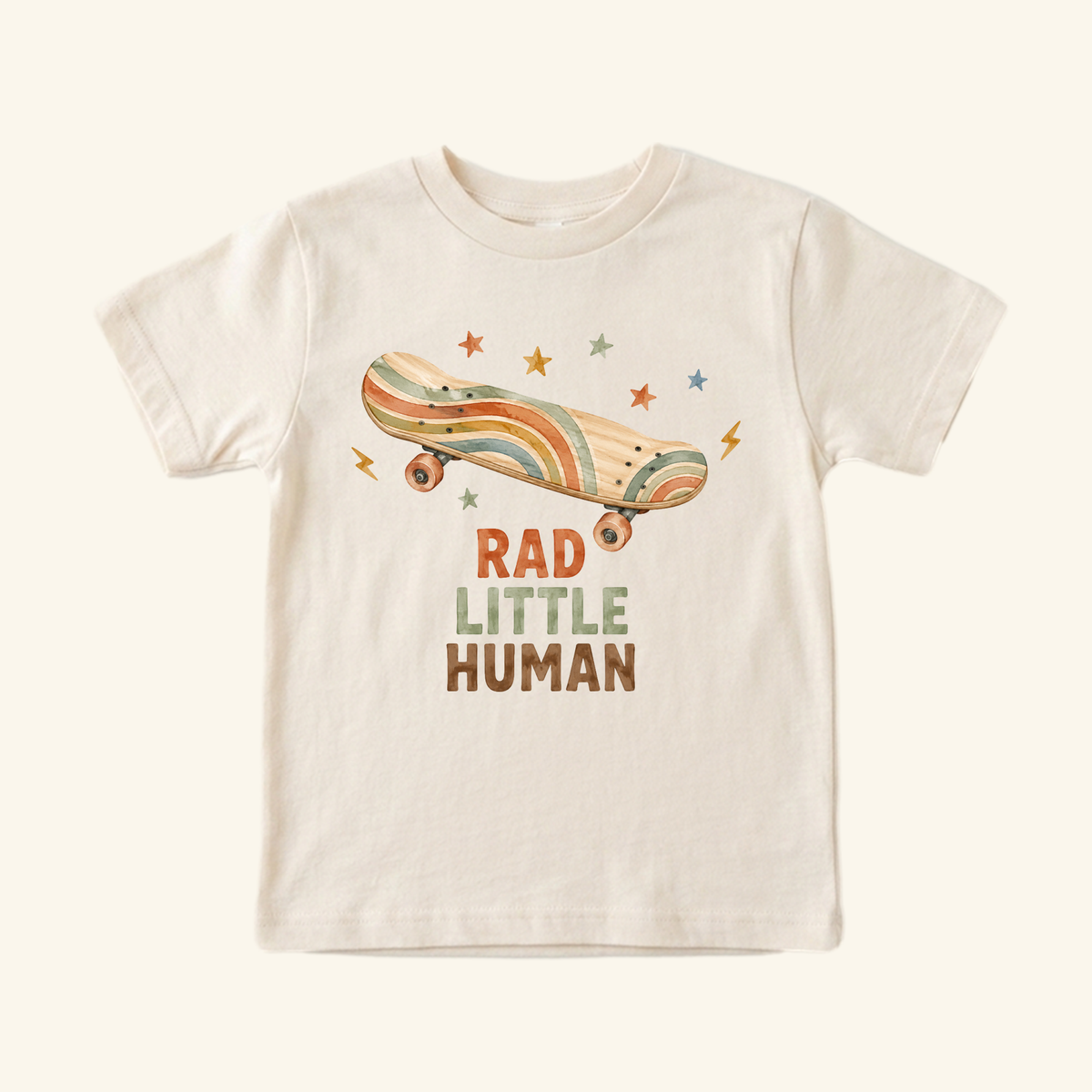 Skateboard Toddler Shirt – Rad Little Human Retro Tee in cream, featuring a short-sleeved design with a retro illustration of a skateboard, stars, and lightning bolts, finished with the text RAD LITTLE HUMAN.