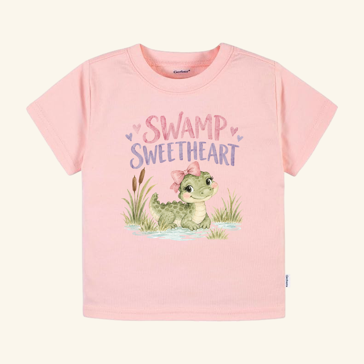 Swamp Sweetheart Toddler Shirt – Baby Alligator Girls Tee in light pink featuring a graphic of a gator wearing a pink bow, surrounded by swamp reeds and the text Swamp Sweetheart.
