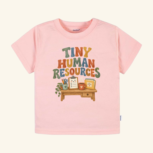 Light pink Tiny Human Resources Toddler Shirt – Funny HR Pun Tee featuring a graphic of a desk with a clipboard, a mug, and a plant.