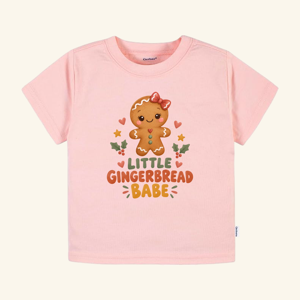 Light pink Toodleroos Little Gingerbread Babe Toddler Shirt featuring a gingerbread person with a red bow and the text LITTLE GINGERBREAD BABE.