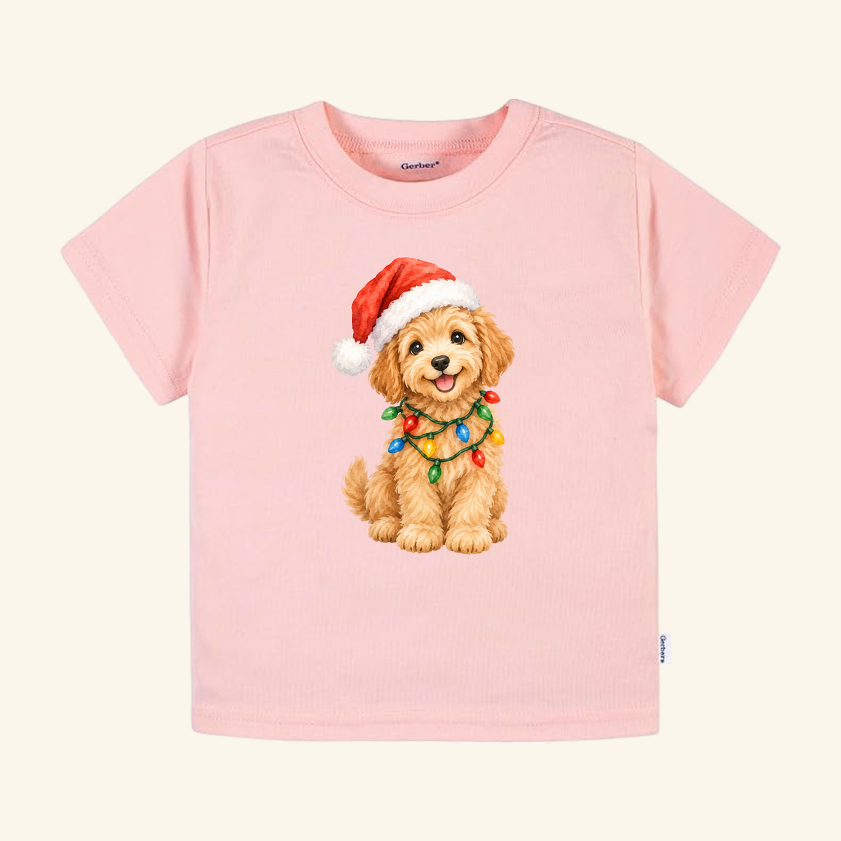 Light pink Christmas Puppy Toddler Shirt – Cute Goldendoodle Holiday Tee featuring a puppy wearing a Santa hat and wrapped in colorful Christmas lights.