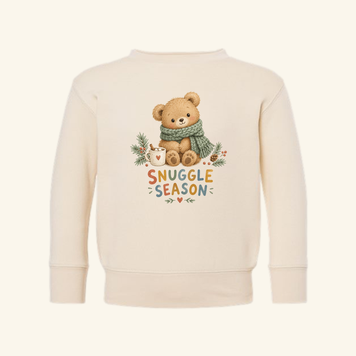 Snuggle Season Toddler Sweatshirt – Cozy Winter Teddy Bear Pullover in cream, featuring a graphic of a teddy bear wearing a green scarf and holding a mug of cocoa with the text SNUGGLE SEASON.
