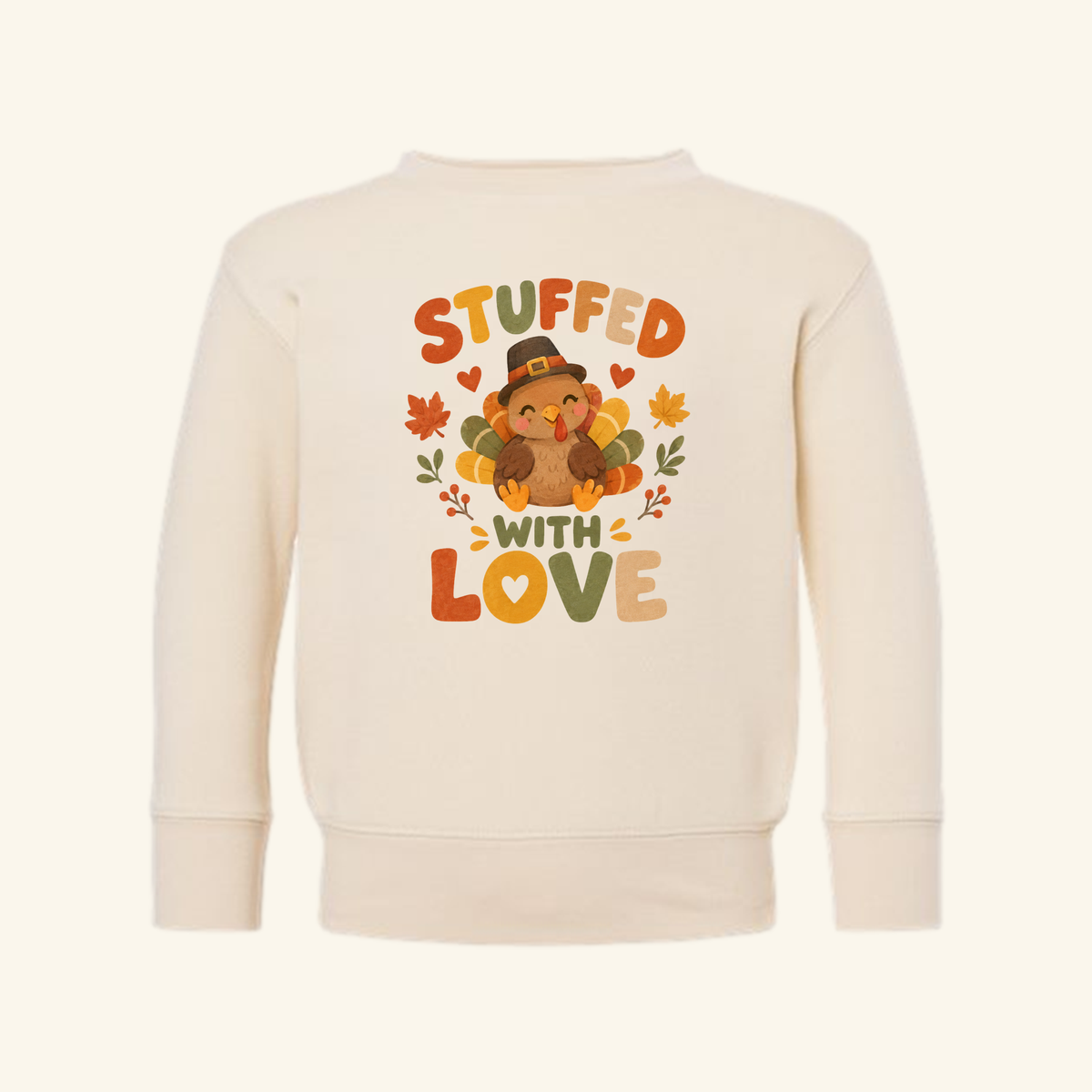 Cream-colored Stuffed With Love Toddler Sweatshirt – Thanksgiving Turkey Pullover featuring a cartoon turkey in a hat, surrounded by fall leaves and the text STUFFED WITH LOVE.