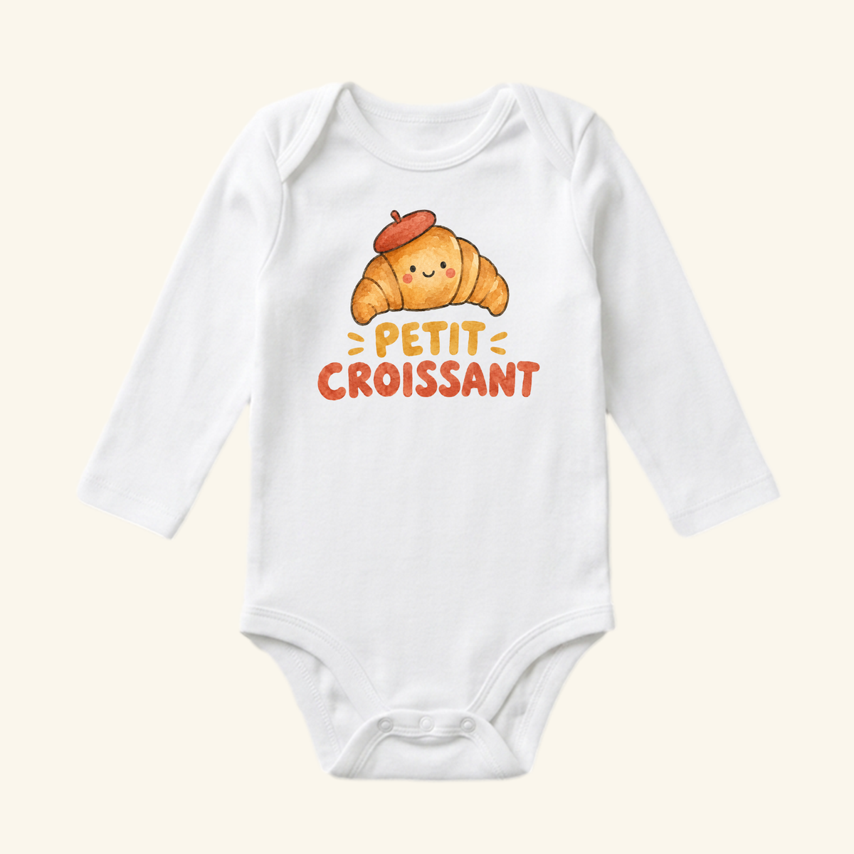 White long-sleeve Petit Croissant Baby Onesie featuring an illustration of a smiling croissant wearing a red beret, with the text PETIT CROISSANT printed below.