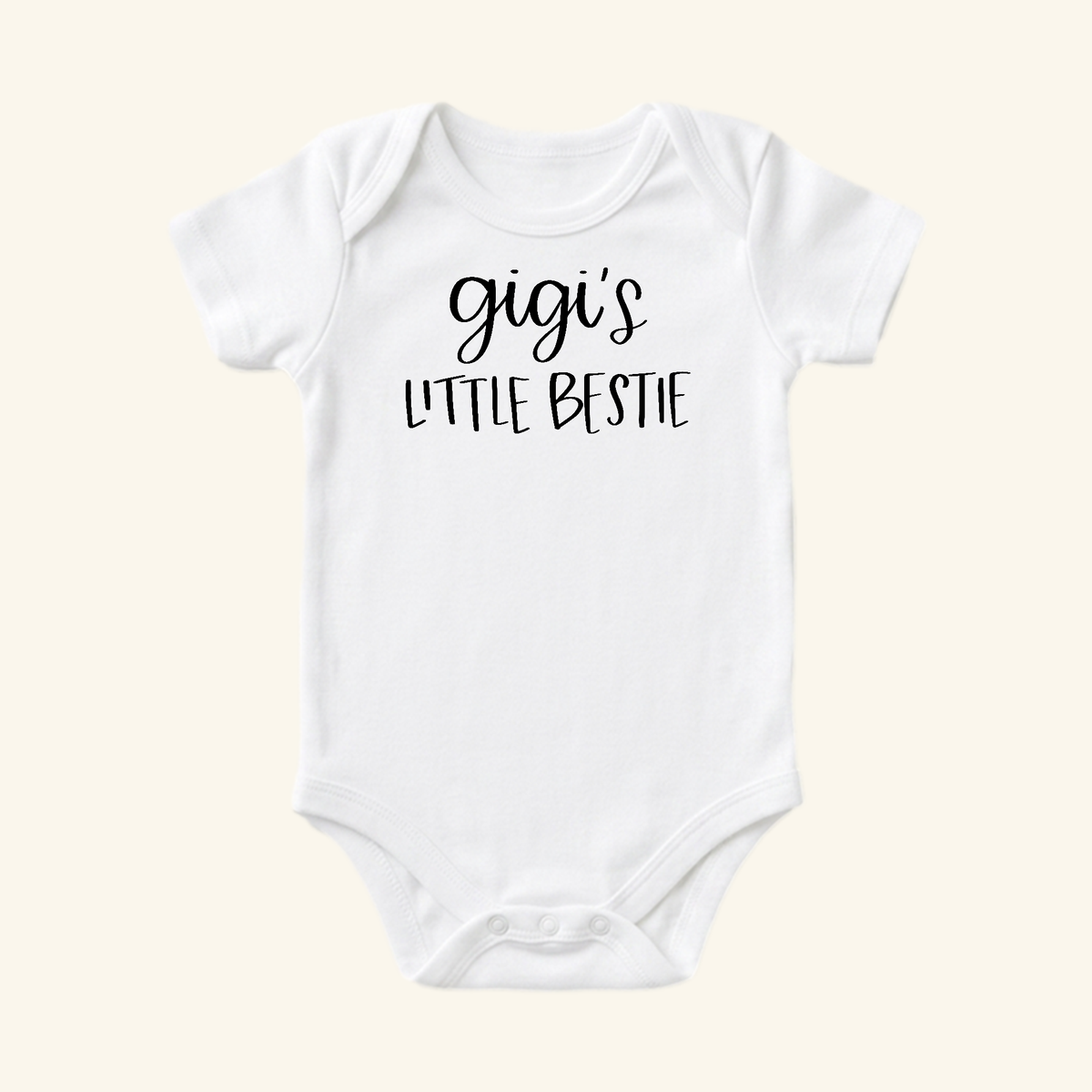White short-sleeved Gigi Baby Onesie – Gigi’s Little Bestie Bodysuit with Gigi’s Little Bestie printed in black on the chest.