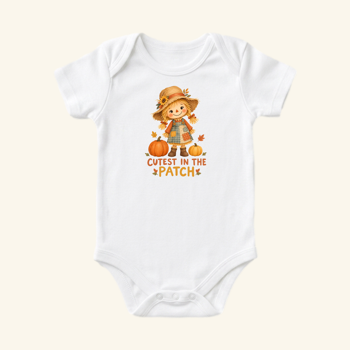 Toodleroos Cutest in the Patch Baby Onesie featuring a white bodysuit with a scarecrow girl and pumpkins, accompanied by the text CUTEST IN THE PATCH.