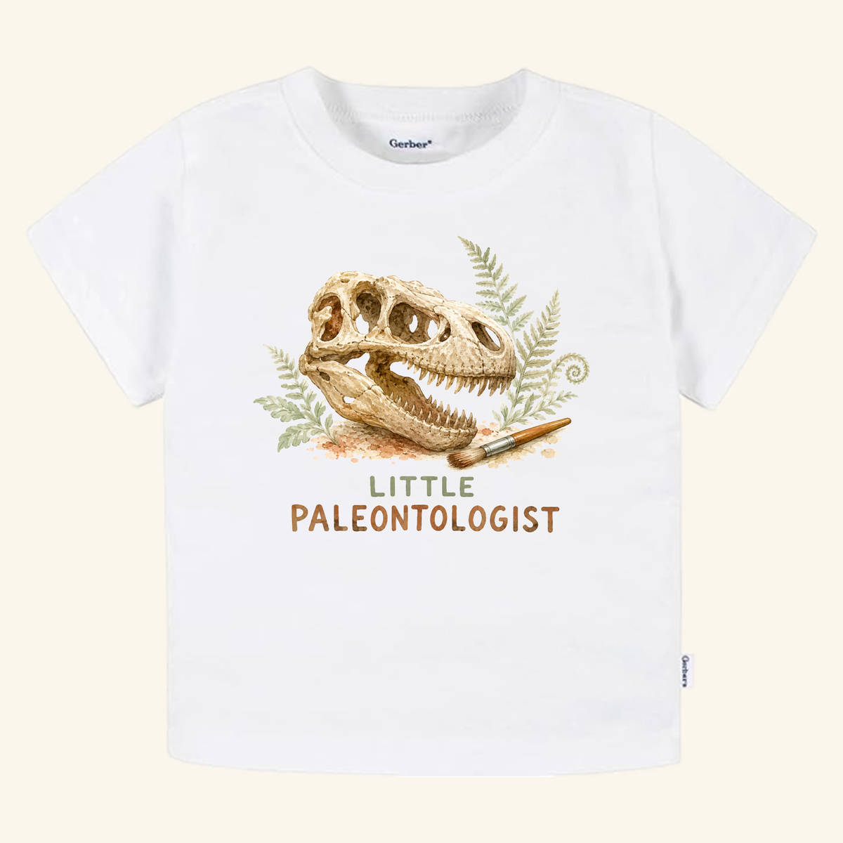 White Little Paleontologist Toddler Shirt – T. Rex Fossil Dinosaur Tee featuring an illustration of a skull, a paintbrush, and ferns, with the text LITTLE PALEONTOLOGIST printed below.