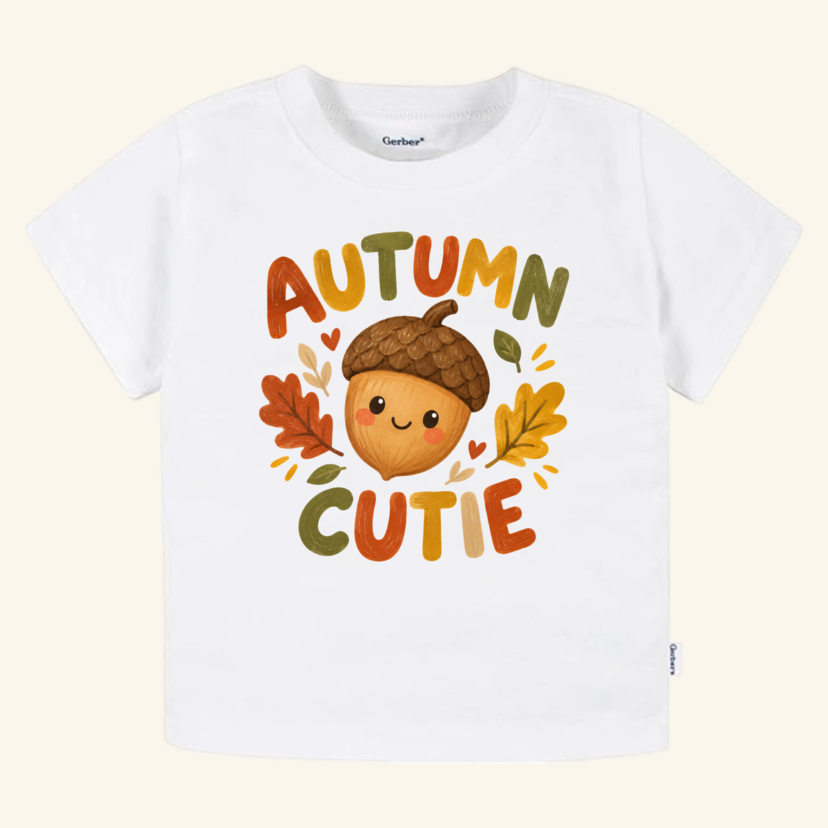 White Autumn Cutie Acorn Toddler Shirt featuring a cartoon acorn character surrounded by fall leaves and the text AUTUMN CUTIE.