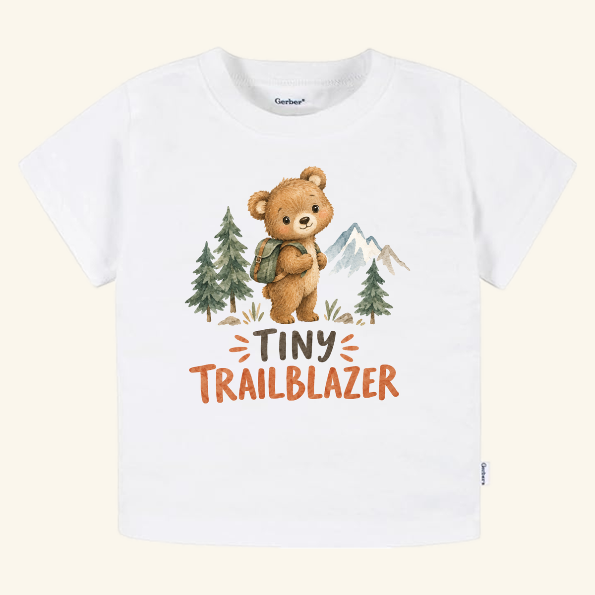 White Tiny Trailblazer Toddler Shirt – Hiking Bear Adventure Tee featuring a watercolor illustration of a bear with a backpack among pine trees and mountains, with the text Tiny Trailblazer below.