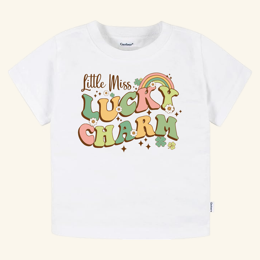 Toodleroos St. Patrick’s Day Toddler Shirt – Little Miss Lucky Charm featuring a retro graphic in colorful bubble letters, decorated with a rainbow, flowers, and shamrocks on a white t-shirt.