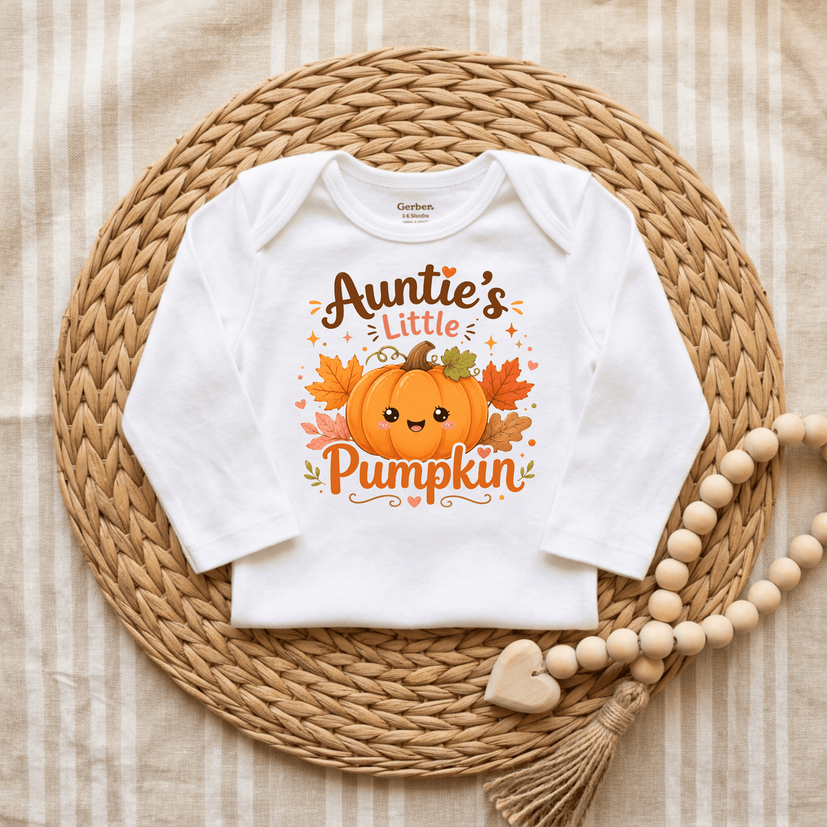 Dress your little one in the Toodleroos Auntie’s Little Pumpkin Baby Onesie – Fall Pumpkin Bodysuit, featuring an adorable pumpkin and autumn leaves design with the phrase “Auntie’s Little Pumpkin.” Displayed on a woven mat beside a wooden beaded garland, this is the perfect fall baby bodysuit or pumpkin patch outfit for the season.