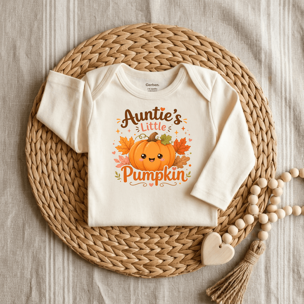 Dress your little one in this cream Auntie’s Little Pumpkin Baby Onesie – Fall Pumpkin Bodysuit by Toodleroos, featuring a sweet pumpkin graphic and “Auntie’s Little Pumpkin” text. Styled on a woven placemat with a charming beaded heart accent, it makes the perfect adorable fall baby outfit or first pumpkin patch look.