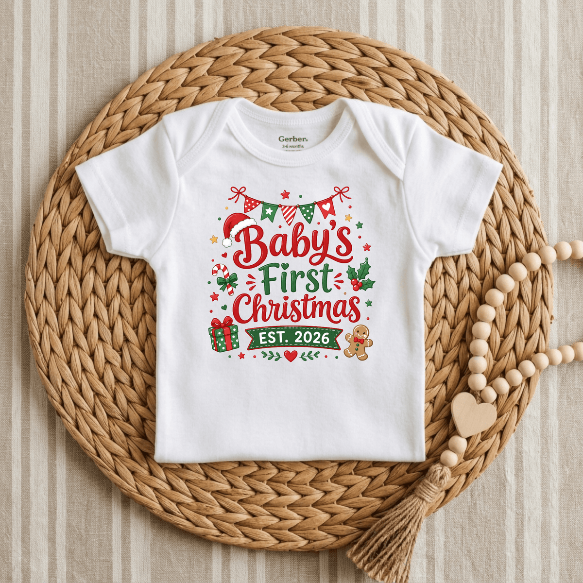 A white Baby’s First Christmas Est. 2026 Long Sleeve Onesie by Toodleroos is displayed on a woven mat, featuring festive holiday decorations, a gift, gingerbread man, and beads with a wooden heart nearby. This charming holiday keepsake bodysuit is the perfect 2026 Christmas outfit for your little one’s memorable first celebration.
