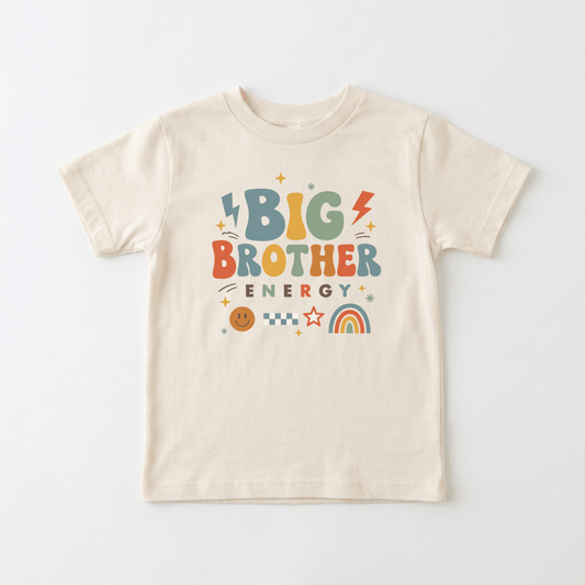 Dress your toddler in the Toodleroos Big Brother Energy Toddler Shirt – Retro Graphic Design, featuring a beige base with colorful lettering that says “Big Brother Energy” and fun graphics like lightning bolts, stars, a rainbow, checkerboard pattern, and a smiley face—ideal for celebrating your little one as a big brother or making an adorable pregnancy announcement.