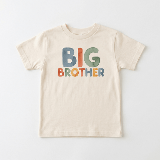 The Toodleroos Big Brother Toddler Shirt – Colorful Retro Design features bold, vibrant “BIG BROTHER” lettering across the front of a beige shirt, laid flat on a white background—perfect as a fun big brother shirt or a memorable pregnancy announcement shirt.