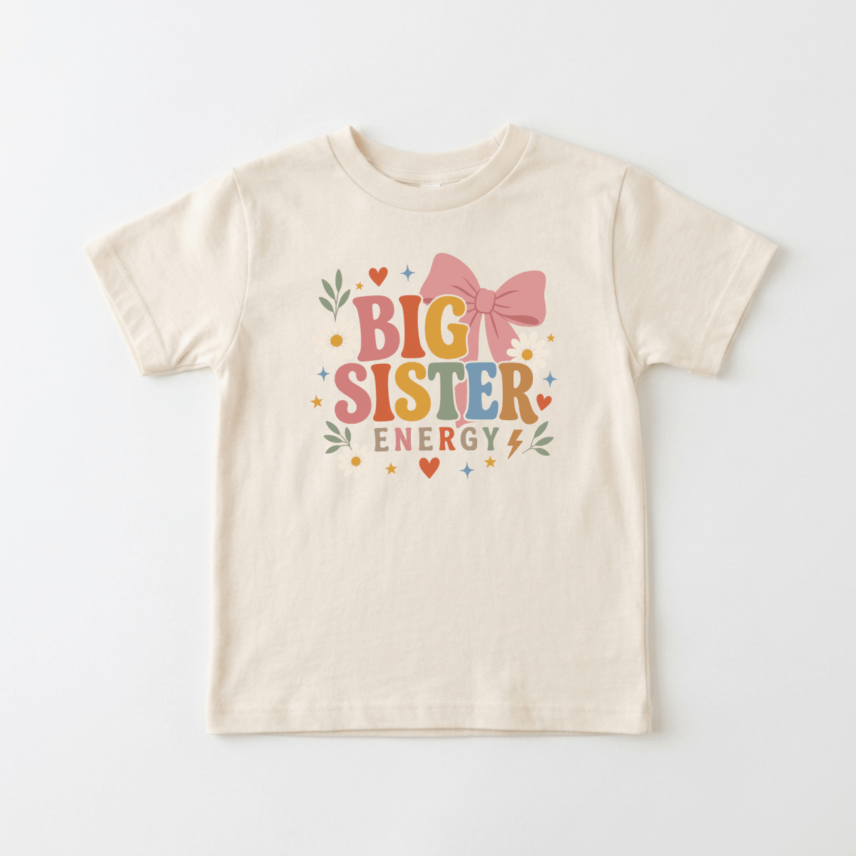 Introducing the Toodleroos Big Sister Energy Toddler Shirt – Retro Floral Design: a beige tee featuring vibrant “BIG SISTER ENERGY” text, adorned with a bold pink bow, hearts, stars, leaves, and a lightning bolt—making it the perfect fun pregnancy announcement or an adorable big sister outfit for your toddler.