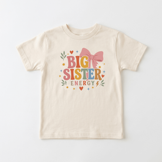 Introducing the Toodleroos Big Sister Energy Toddler Shirt – Retro Floral Design: a beige tee featuring vibrant “BIG SISTER ENERGY” text, adorned with a bold pink bow, hearts, stars, leaves, and a lightning bolt—making it the perfect fun pregnancy announcement or an adorable big sister outfit for your toddler.